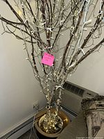 Full view of lighted decorative tree with white and brown branches in gold pot.
