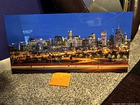Full front view of the Denver city skyline at night photograph measuring 10x20 inches set against a carpeted floor and dark wall.