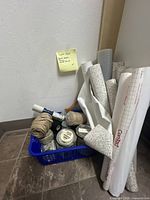 Basket with shelf liners rolled up and multiple cans and balls of twine inside on floor corner