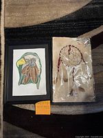 Framed Native American eagle feather picture and packaged dreamcatcher on carpet, side by side.