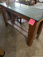 Front and side view of wooden entry table with clear glass top and lower shelf, placed on carpeted floor.