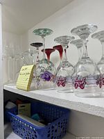 Shelf displaying various themed wine glasses including printed and painted designs, arranged in a row.