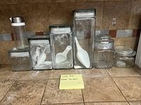 Wide view of six glass canisters on kitchen counter showing sizes and overall condition.