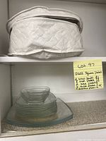 Stack of clear glass square plates and two small square glass bowls on top in kitchen cabinet.