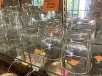 View from top showing rows of clear rounded square glasses in two sizes on a glass shelf with a note indicating 'Water Whiskey glasses'