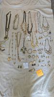Overview of entire lot showing all jewelry items spread on a cloth including necklaces, earrings, rings, pins, and eyeglass cords.