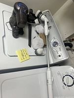 Photo showing Greenote cordless vacuum cleaner and multiple brush attachments for Jumbo scrubber placed on a dryer top in a laundry room.