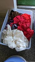 Plastic container with assorted colored fabric hair scrunchies, mainly white, red, and brown