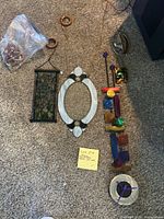 Four stained glass hanging art pieces arranged on carpet: black framed green and brown panel, white oval frame, tall colorful geometric piece, and silver-framed wall clock with purple hands.