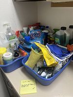 Wide view showing various cleaning supplies including bottles, sprays, gloves and sponges in blue bins.