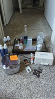 Full lot overview showing two ultrasonic jewelry cleaners, perfumes, lotion, cologne, and cross necklaces arranged on carpet