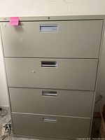 Front view of the large four drawer metal filing cabinet. Light gray color with label holders on each drawer and a lock on the top drawer.