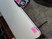 Top view of white foldable table surface with slight surface scuffs and dirt marks, featuring folding leg seen at right side.