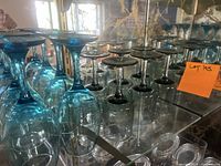 Photo showing four inverted light blue wine glasses with rounded bowls and long stems, arranged on a glass shelf.