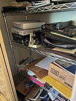 Front view of metal wire shelving unit filled with various items including books, cardboard boxes, folders, binders, and a small microscope.