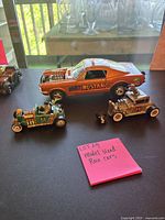 Overview of three model race cars including Mighty Mustang, Fast Frankie, and Werewolf Coupe on black surface with note pink sticky note