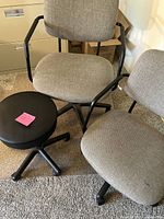 Three office chairs, two with armrests and one with wheels, and one black adjustable stool with wheels on carpeted floor.