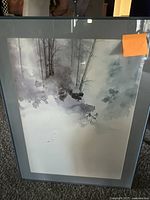 Framed watercolor painting showing skiers in a misty, snowy forest scene. The framing includes a glass cover and grey matting. The size of the artwork is 32x24 inches as provided by the seller.