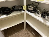 Shelf with several pots with glass lids and frying pans, showing cookware variety and storage condition.