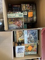 Two open boxes containing multiple boxed jigsaw puzzles with visible box art and piece count labels, mostly 300 pieces