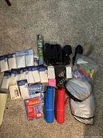 Wide view of all rain gear items arranged on carpet: multiple sealed rain ponchos, compact umbrellas, emergency blankets, and miscellaneous gear in plastic bags.