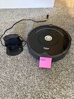 Black iRobot Roomba vacuum cleaner with charging base on carpet surface, front angle.
