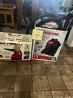 Photo showing boxed Shop Vac and Scunci steamer placed side by side on tile floor in a kitchen setting.