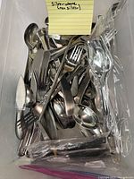 Photo of assorted flatware including forks, spoons, and spreaders loosely arranged in a container, with a note indicating non-silver flatware.