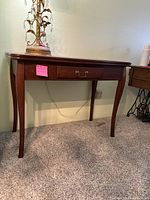 Front view of wooden sofa/entryway table showing tapered legs and central decorative drawer with brass handle under curved tabletop.