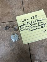 Photo of all items in the lot showing the jade elephant pendant, sterling silver ring, and sterling silver earrings next to a handwritten note describing the lot contents.