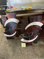 Two abstract stone art sculptures placed side by side on carpeted floor with wooden bench behind.