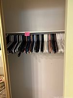 Full view of a closet rod densely packed with various colors of plastic hangers including white, black, blue, beige, and a few pink ones.
