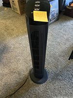 Front view of a tall black tower fan showing the control buttons on top and fan grill running vertically.
