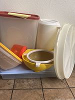 Assortment of plastic containers including bowl with red lid, small containers, yellow strainer, and collapsible white strainers