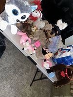 Photo of table with assortment of stuffed animals including husky dog, bears, Minnie Mouse, elephant and small pink plush toys