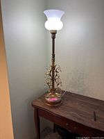Full view of the vintage table lamp illuminated, showing the frosted glass shade, twisted gilt column, and crystal decorations.