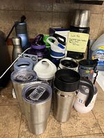 Wide view showing full collection including water bottles, travel mugs, and thermos with koozie on a kitchen countertop.