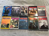 40-piece collection of DVDs and Blu-rays showing a collection of TV series including multiple Sopranos seasons and Alias.