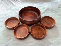Top view of one large serving bowl surrounded by four smaller bowls, showing the warm brown stained maple wood with visible grain and smooth finish.