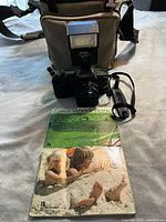 Canon 35mm SLR film camera with attached Canon FD 50mm f/1.8 lens, lens cap, Vivitar 2600D flash mounted on camera, camera strap, carrying bag, and photography booklets