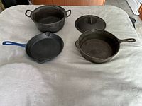 Photo showing the full set of 2 cast iron skillets and 1 Dutch oven with lid on a white cloth surface
