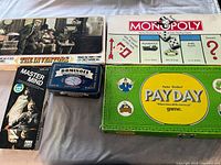 Five classic board games and a dominoes set displayed, showing The Inventors, Monopoly, Payday, Master Mind, and Dominoes boxes.