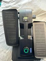 Top view showing the two large textured pedals, central body with electronic display and control button, black finish with teal accent on resistance knob.