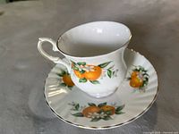 Cup and saucer set featuring bright orange Florida Oranges and floral motifs with gold trimming seen from side angle
