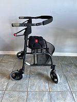 Side view of the foldable black rollator walker showing handlebars with brake levers, padded seat, and storage basket.