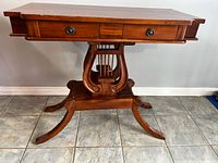 Front view of wooden table showing two drawers and lyre-shaped pedestal base with carved legs.