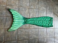 Full length photo of the green mermaid tail laid flat on tiled floor showing scale pattern and fin details