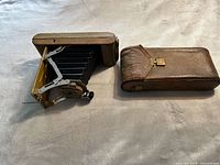 Photo showing the Kodak folding bellows camera fully opened and leather carrying case side by side on a surface.
