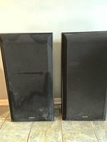 Front view of speakers with grilles attached, showing black fabric covering and overall rectangular shape with Pioneer logo on grille.