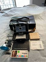 Full contents including camera, case, strap, flash, film and accessories laid out on fabric surface.